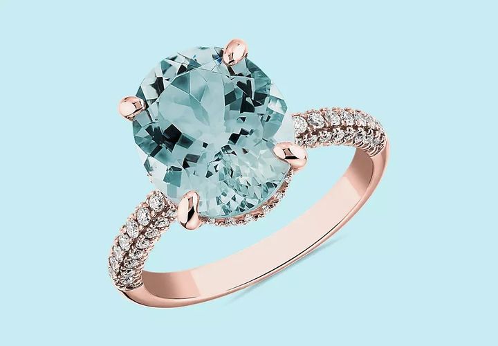 A March birthstone cocktail ring featuring 12 millimeter by 10 millimeter aquamarine oval cut center accented by two rows of pavé diamonds through the rose gold shank